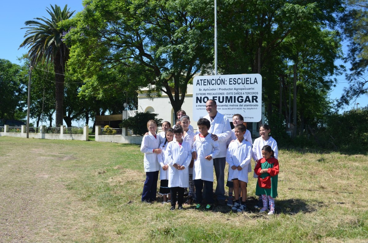 Docente y alumnos de una escuela rural frente al cartel de advertencia